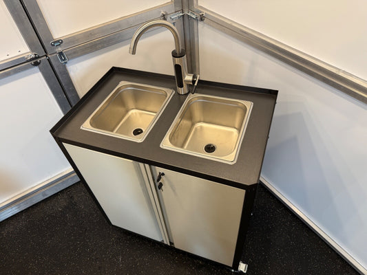 A portable hot water sink double unit with a stainless steel surface, two sinks, a faucet, and a lockable cabinet with caster wheels for mobility.