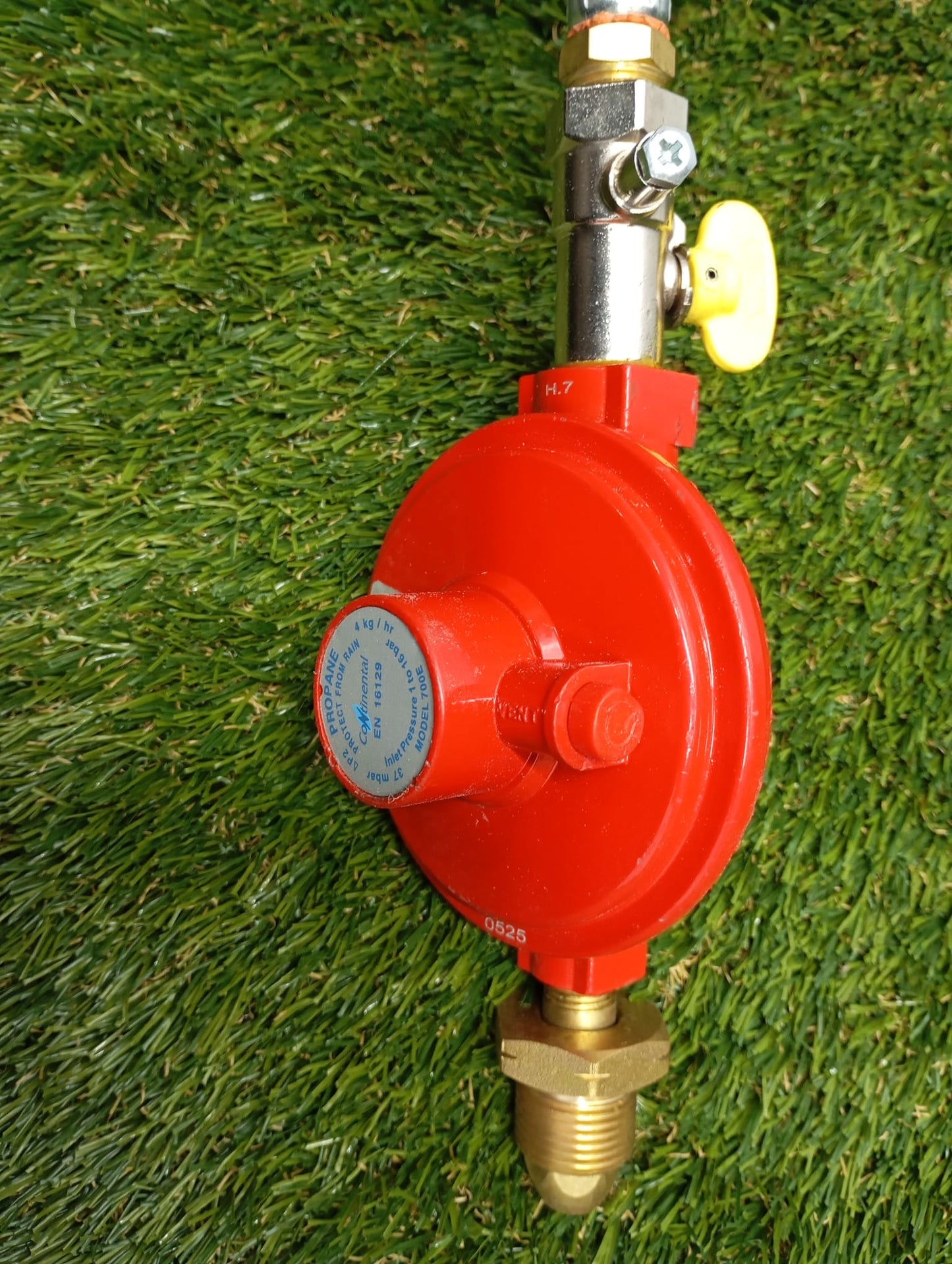 Red pressure gauge with brass connectors on a grass background