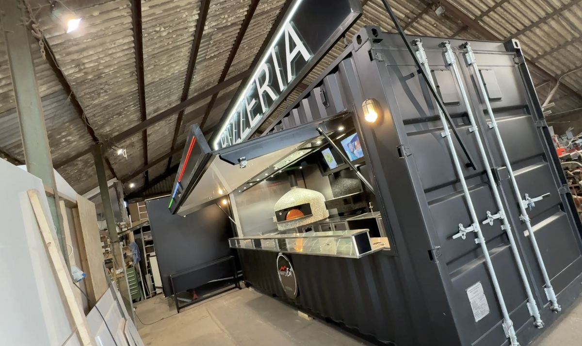 Pizzeria setup inside a large container with a wood-fired oven.