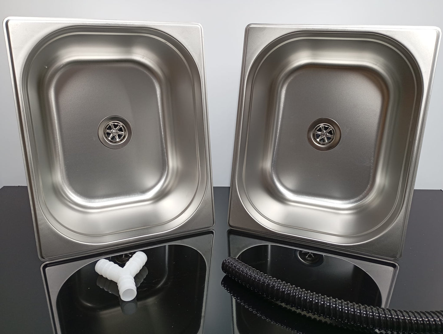 Two stainless steel sinks on a reflective surface with a neutral background