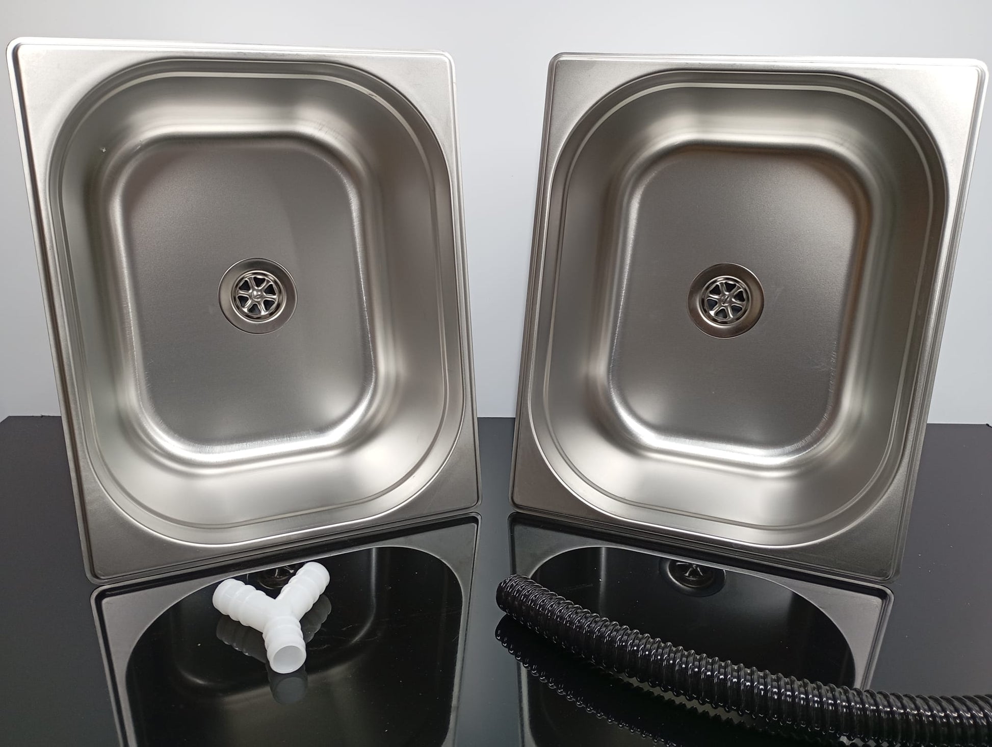 Two stainless steel sinks on a reflective surface with a neutral background